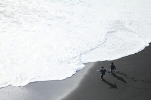 Two kids running near the surf at Reynisfjara black sand beach in Iceland