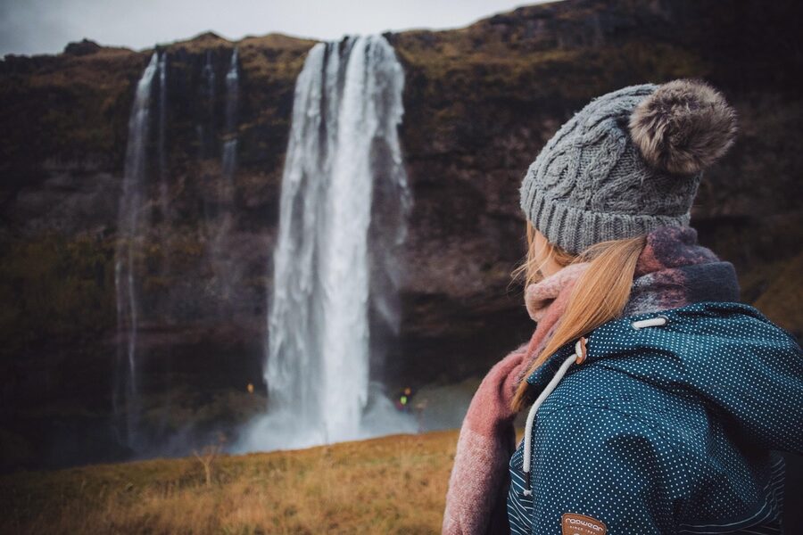 Hiker in warm layers and a beanie next to an Icelandic waterfall