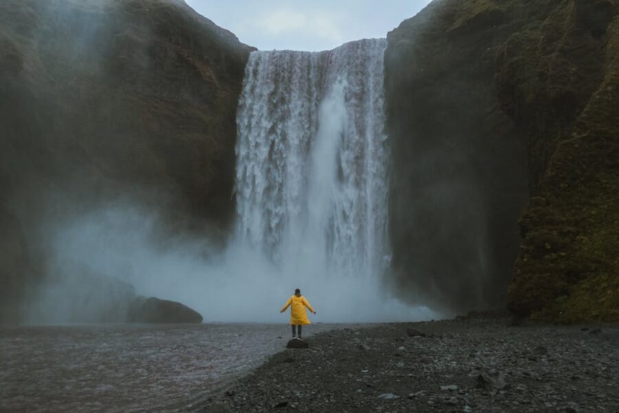 Person in a yellow waterproof coat at Skogafoss waterfall in Iceland