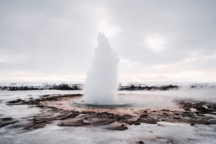 Strokkur geyser erupting in winter against a snowy backdrop