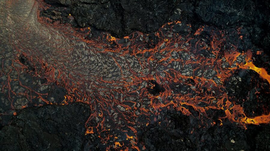 Glowing magma flowing across dark Iceland landscape at night