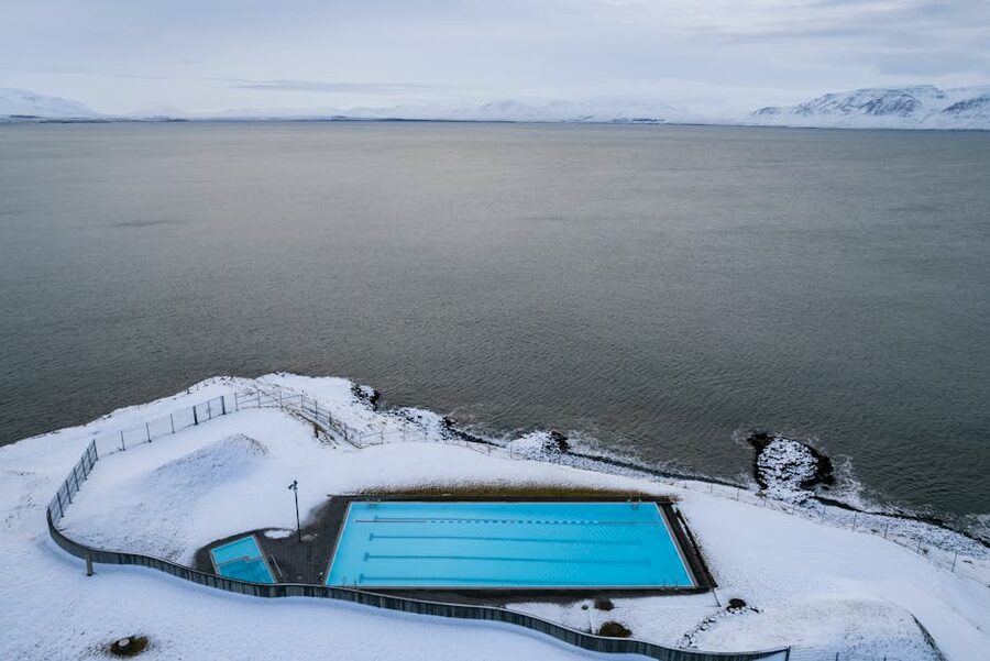 Aerial view of a snow-rimmed swimming pool by the ocean in Hofsos Iceland
