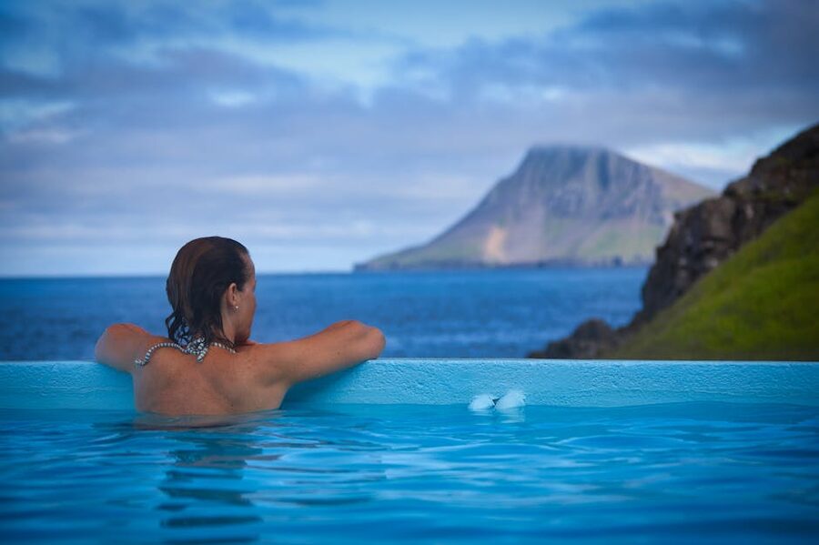 Back view of a woman relaxing in an outdoor thermal pool with Icelandic mountains