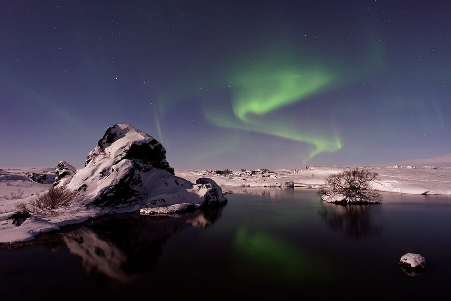 Aurora reflecting in a still Iceland lake under a mountain skyline