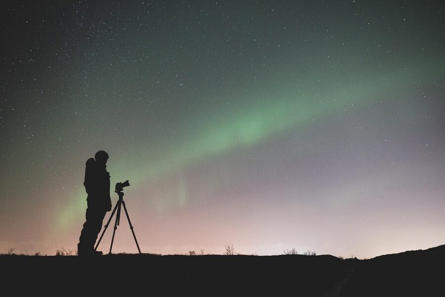 Photographers and tripods set up under a green aurora in Iceland