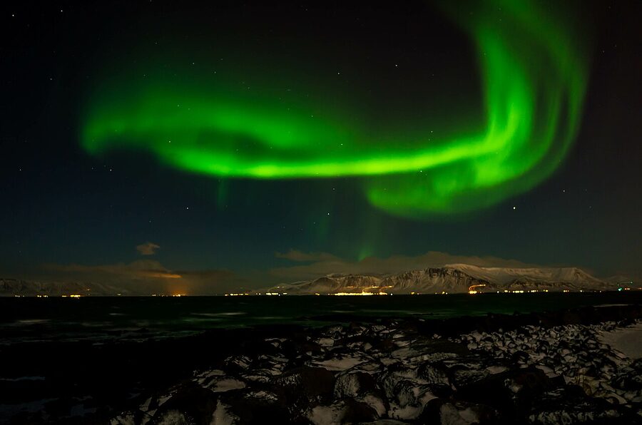 Aurora arch over the lit-up rooftops of Reykjavík city