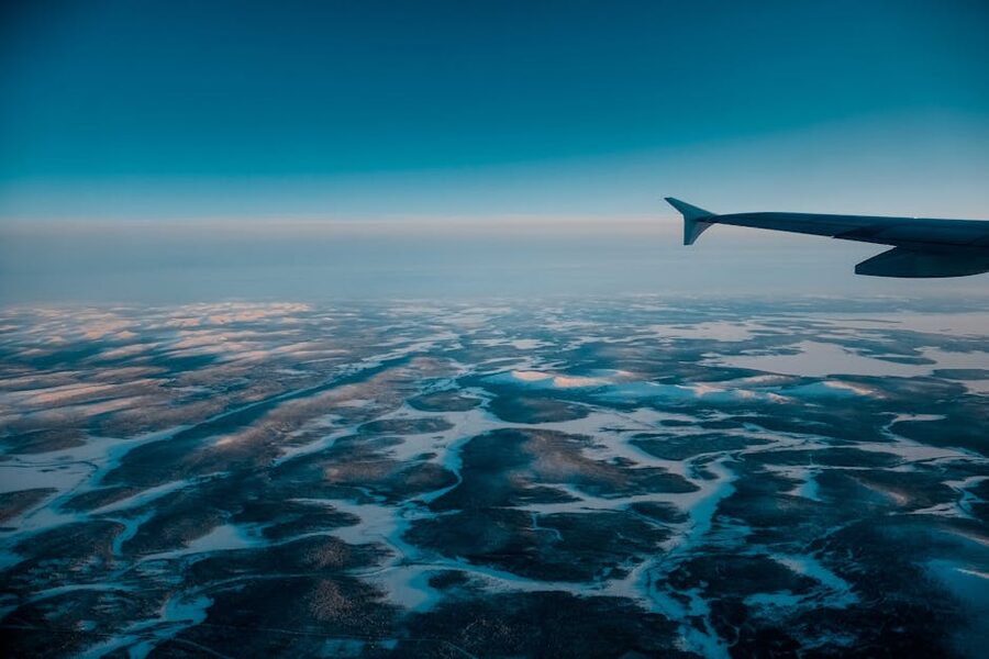 Aircraft wing flying in clear blue sky over snow-covered terrain