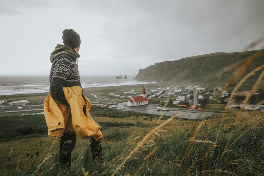 Person in warm clothing overlooking Vík, Iceland in misty landscape