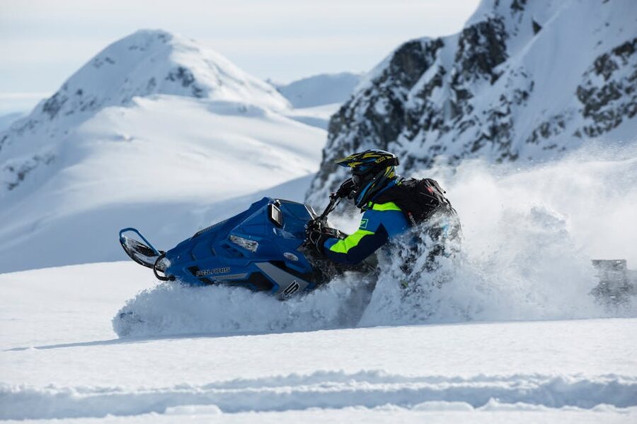 Person riding a snowmobile across a snowy mountain landscape