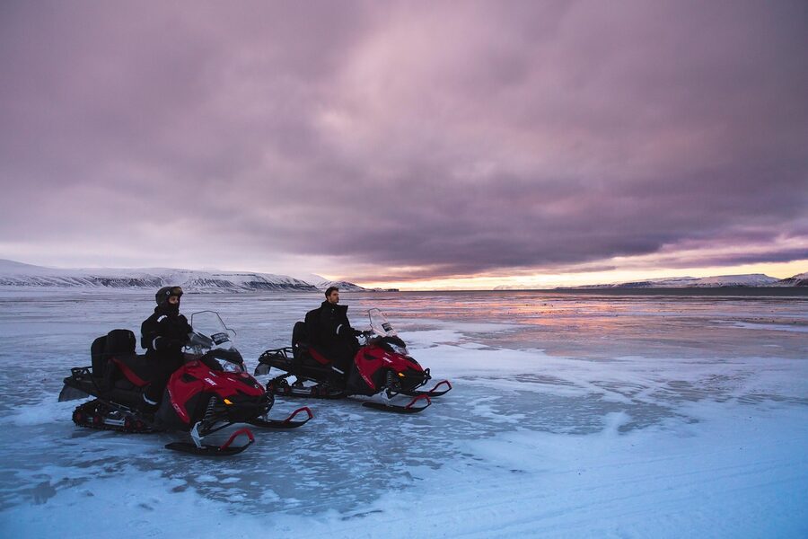 Three snowmobiles riding in line across snowy glacier landscape