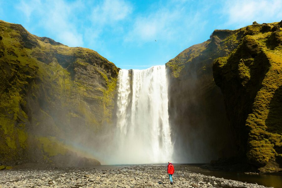 Visitor in a red coat at the base of Skogafoss waterfall