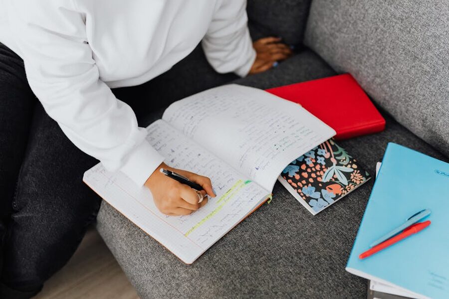 Person writing in a notebook with an open book