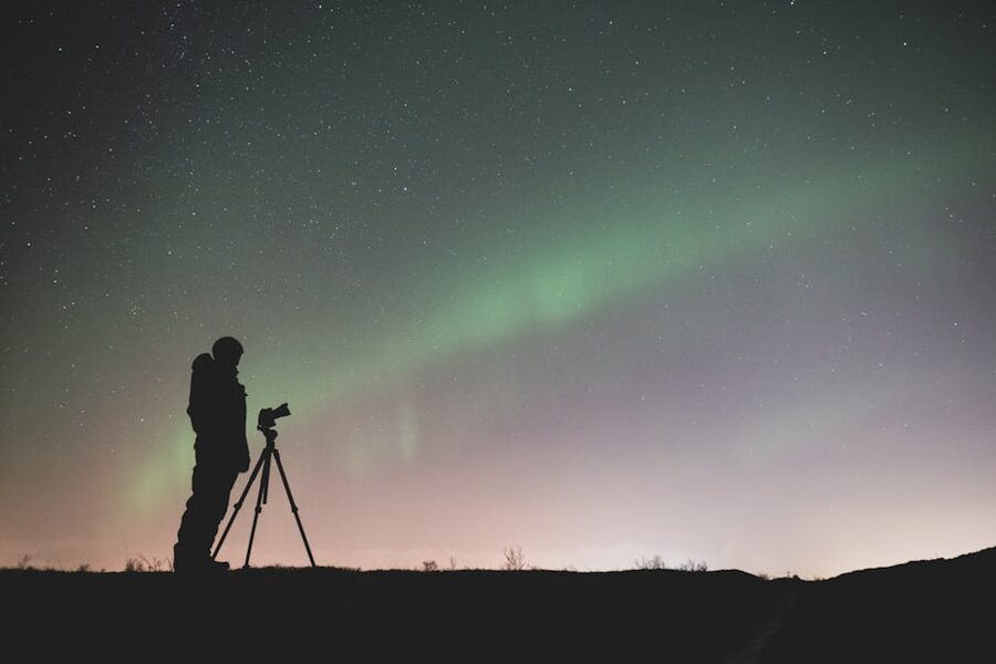 Photographer with tripod under green aurora and starry sky in Iceland