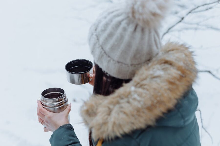 Person with thermos in snowy landscape, dressed for aurora